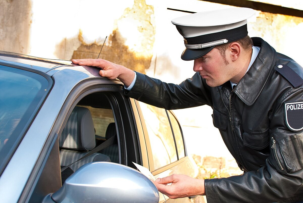 Polizist kontrolliert einen Autofahrer und nimmt dessen Dokumente entgegen.