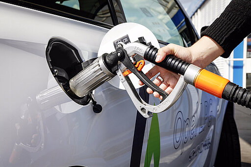 Eine Person betankt ein Auto an einer Tankstelle mit Flüssiggas (LPG) und hält die Zapfpistole sicher in den Tankstutzen des Fahrzeugs.