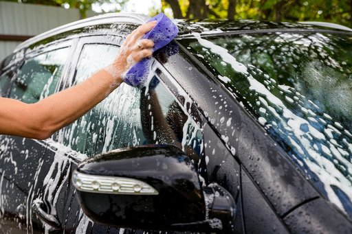 Eine Person wäscht ein schwarzes Auto