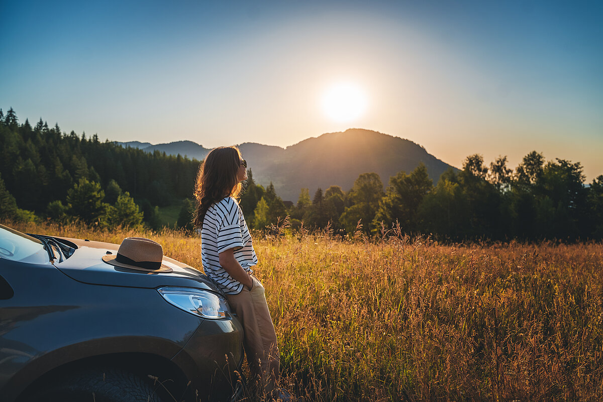 Junge Frau lehnt an motorhaube eines autos in der natur