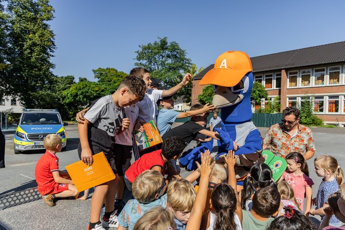 Gruppe von Kindern umringt das Pfau-Maskottchen und einen Polizisten