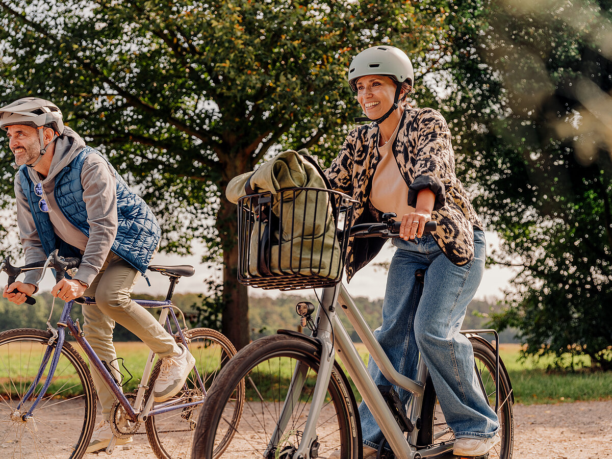 „Ein Pärchen mit Fahrradhelmen fahren nebeneinander auf Fahrrädern durch eine ländliche Umgebung.“