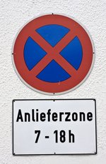 Ein Verkehrsschild mit einem Halteverbotssymbol, das durch einen roten Kreis mit einem blauen Hintergrund und einem roten Kreuz dargestellt wird. Darunter befindet sich ein weißes Zusatzschild mit der Aufschrift ‚Anlieferzone 7 - 18 h