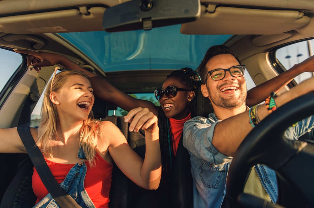 3 junge menschen sitzen lachend in einem auto
